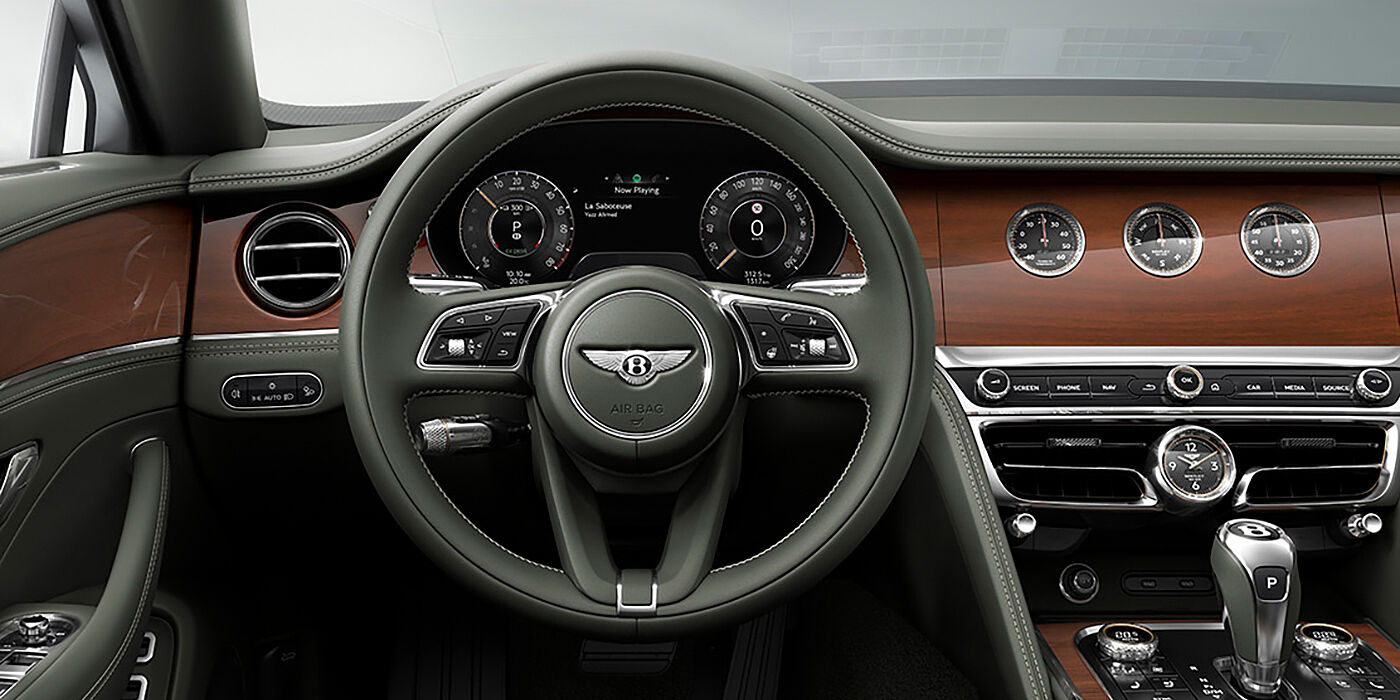 JCT600 Service Teeside New Bentley Flying Spur sedan front cabin in Cumbrian Green hide and Crown Cut walnut veneer showing steering wheel and Rotating Display with three clocks on face