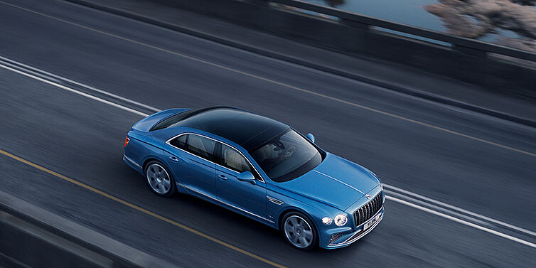 JCT600 Service Teeside New Bentley Flying Spur Azure sedan in Light windsor blue paint by Mulliner, with 22 inch Azure wheels seen from overhead driving dynamically on a country road