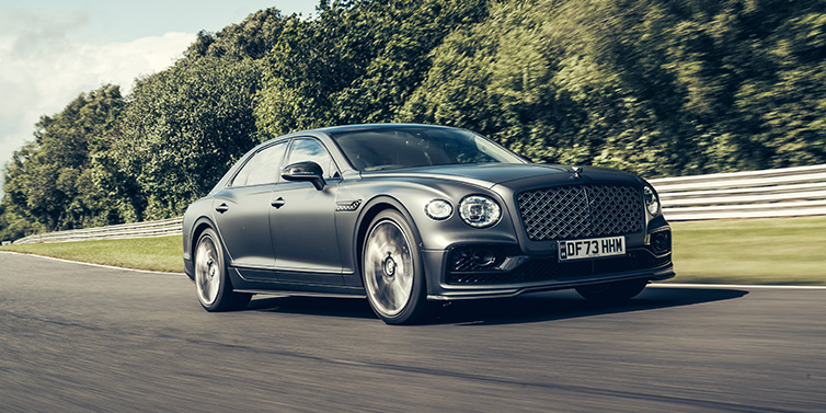 JCT600 Service Teeside Bentley Flying Spur Mulliner sedan front three quarter in dark grey paint driving dynamically by some trees on a track