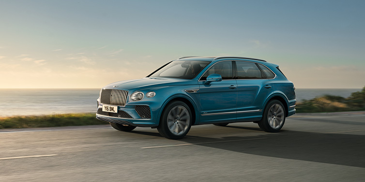 JCT600 Service Teeside Bentley Bentayga Azure SUV in Topaz blue paint driving dynamically by the ocean with 22 inch 10 spoke directional wheels