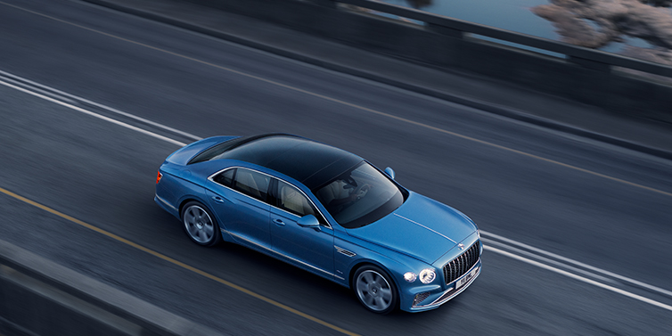 JCT600 Service Teeside New Bentley Flying Spur Azure sedan in Light windsor blue paint by Mulliner, with 22 inch Azure wheels seen from overhead driving dynamically on a country road