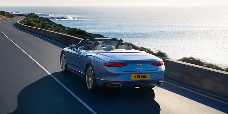 JCT600 Service Teeside New Bentley Continental GTC Azure convertible rear view in Light Windsor blue paint with 22 inch ten spoke wheels driving dynamically on an ocean road in the sunshine