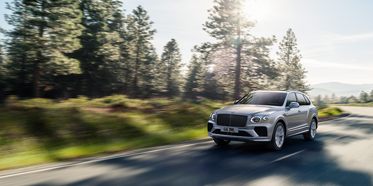 JCT600 Service Teeside Bentley Bentayga SUV front three quarter in Moonbeam silver paint driving dynamically along a tree-lined road