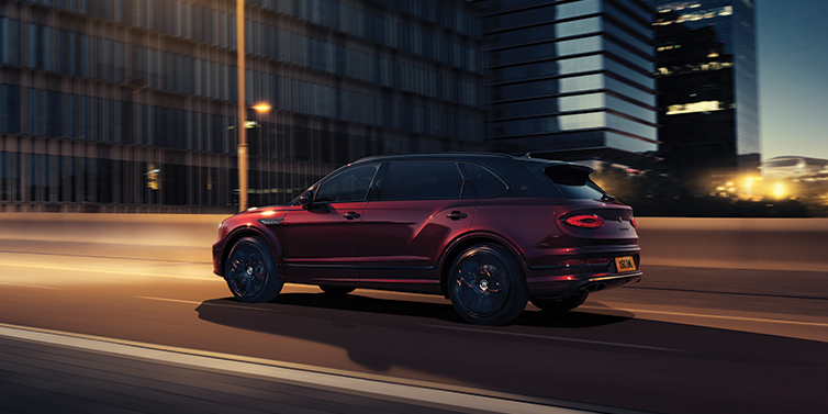 JCT600 Service Teeside Bentley Bentayga Extended Wheelbase Mulliner SUV in Cricket Ball red paint driving dynamically in city at night